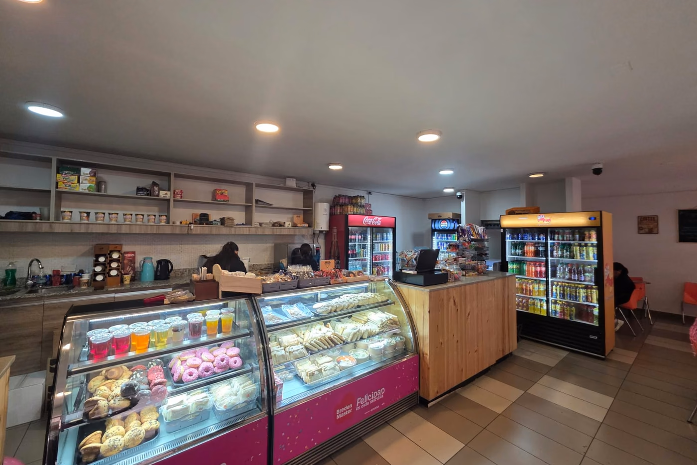 Vista del local: la vitrina de pastelería, el mesón, los refrigeradores de bebidas y la zona de mesas al fondo.